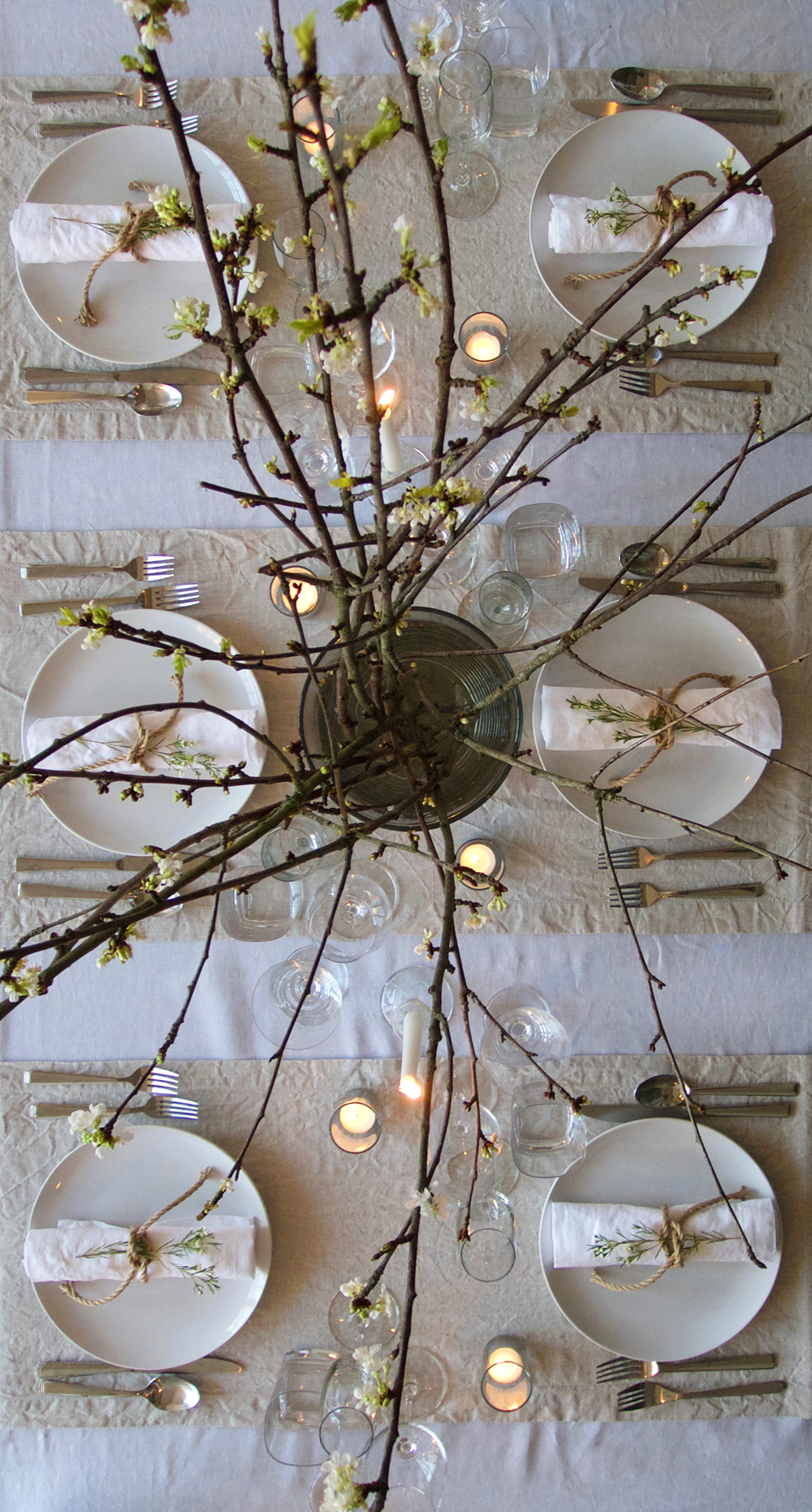Scandinavian dinner party layering white and natural flax linen table linens, candles and blossom